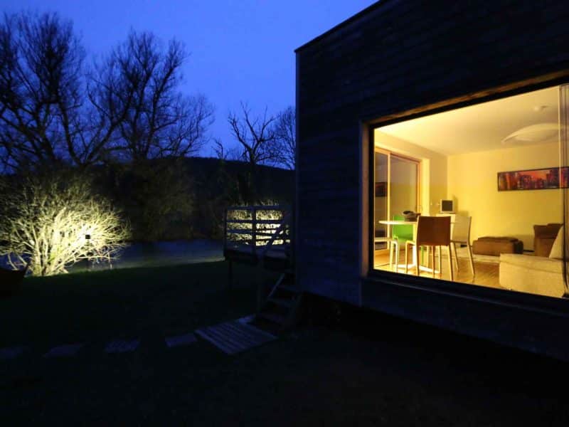 Chalet moderne éclairé la nuit, avec vue sur la nature environnante.
