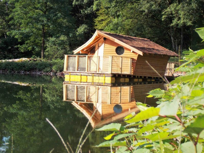 Cabane flottante en bois au bord dun lac, entourée de verdure paisible.