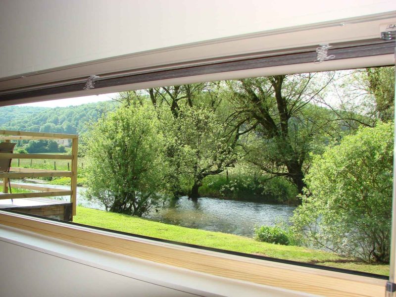 Chalet moderne avec vue sur une rivière et verdure environnante.