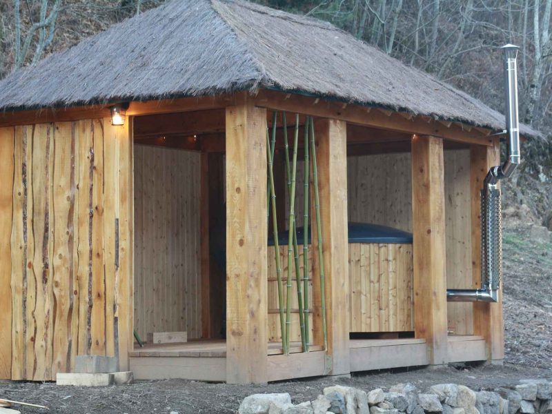 Cabane en bois avec toit de chaume, offrant un spa extérieur relaxant.