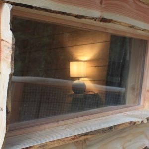 Cabane en bois avec une fenêtre révélant une lampe chaleureuse à lintérieur.