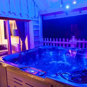 Hébergement insolite en Auvergne-Rhône-Alpes avec jacuzzi lumineux sous un abri en bois.