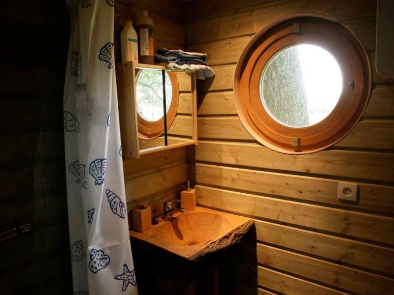 Cabane en bois avec lavabo en pierre et fenêtres rondes, ambiance cosy.