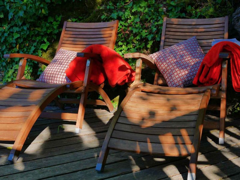 Chaises longues en bois avec coussins colorés, entourées de verdure apaisante.