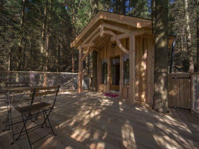 Cabane en bois perchée, entourée darbres, avec terrasse en bois accueillante.