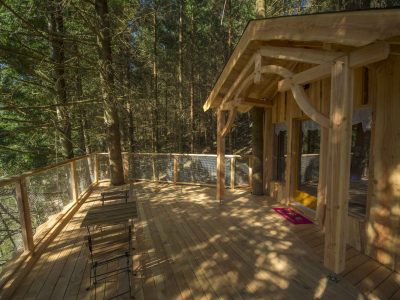 Cabane perchée en bois avec terrasse ensoleillée, entourée darbres.
