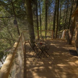 Cabane perchée en bois avec terrasse ensoleillée, entourée de verdure.