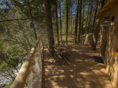 Cabane perchée en bois avec terrasse ensoleillée, entourée de verdure.