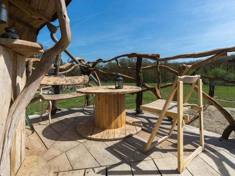 Cabane en bois avec terrasse en rondins et vue dégagée sur la nature environnante.