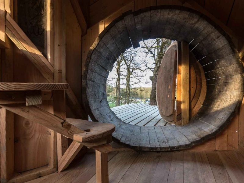 Cabane en bois avec une porte ronde, offrant une vue sur la nature environnante.
