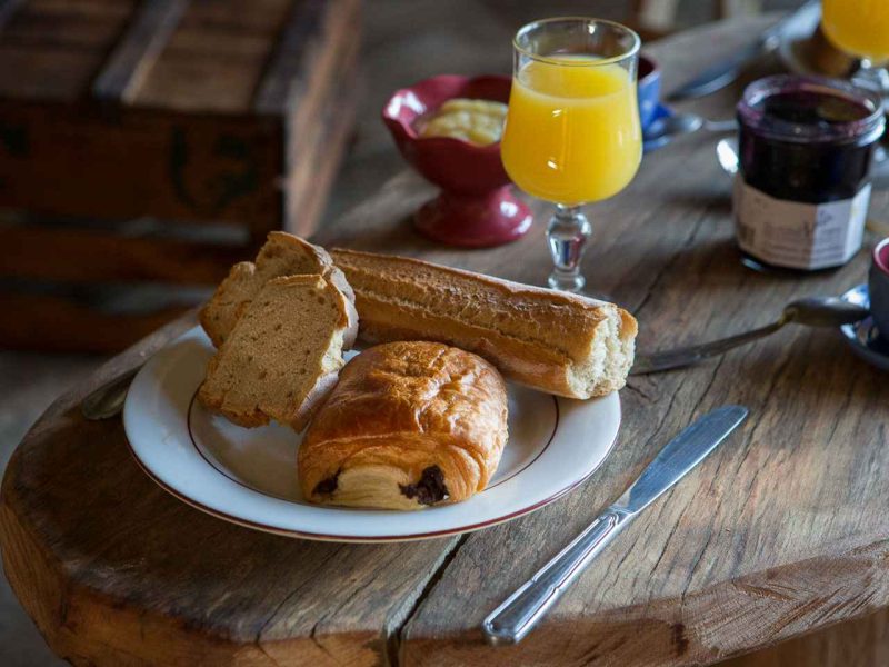 Petit-déjeuner dans un gîte rural : croissant, pain et jus dorange sur une table en bois.