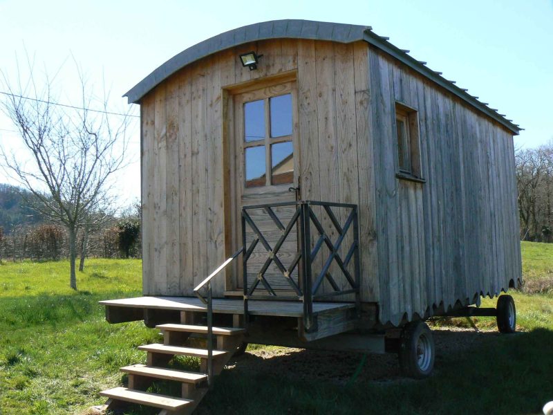 Roulotte en bois à Limousin, avec un accès par des marches en bois et un cadre verdoyant.