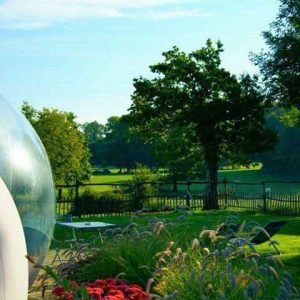 Hébergement insolite en bulle transparente, avec vue sur un jardin fleuri et verdoyant.