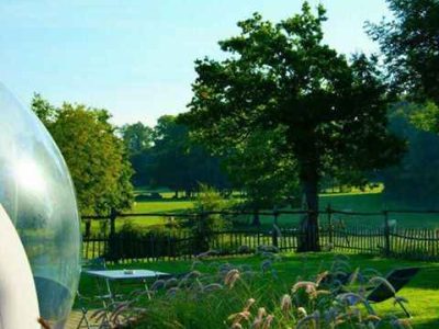 Hébergement insolite en bulle transparente, avec vue sur un jardin fleuri et verdoyant.