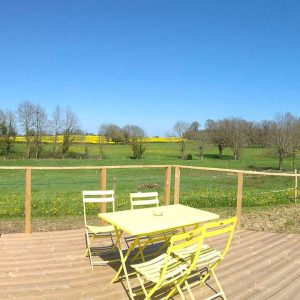 Hébergement insolite en forme de tonneau avec terrasse en bois et vue sur la campagne.