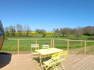Hébergement insolite en forme de tonneau avec terrasse en bois et vue sur la campagne.