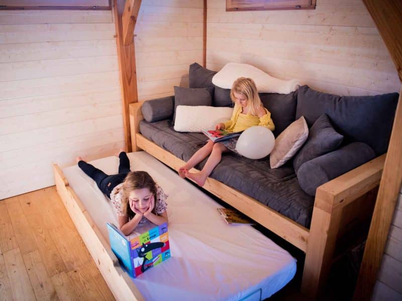Chalet en bois avec enfants lisant sur un canapé confortable et lit dappoint.