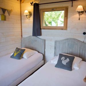 Chalet en bois avec lits jumeaux, décoré de coussins animaliers et lumière douce.