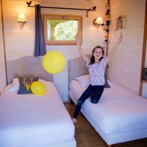 Chalet en bois à Midi-Pyrénées, enfant joyeux avec des ballons jaunes dans la chambre.