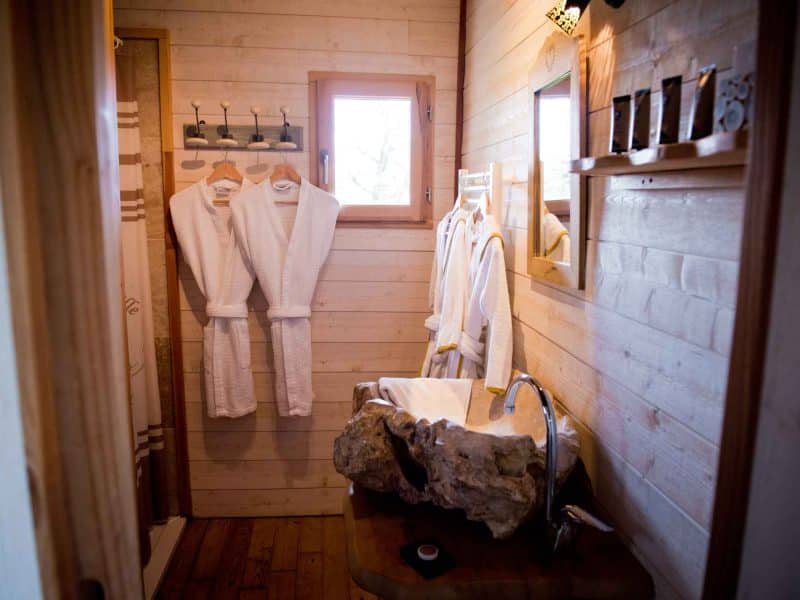 Salle de bain dun chalet en bois, avec peignoirs accrochés et lavabo en pierre.