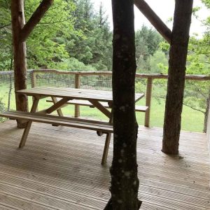 Cabane perchée dans les arbres, avec une terrasse en bois et vue sur la nature.