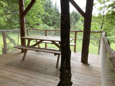 Cabane perchée dans les arbres, avec une terrasse en bois et vue sur la nature.