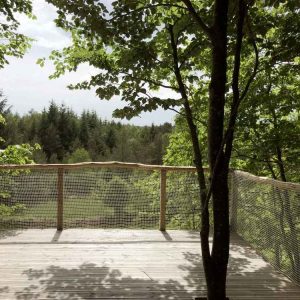Cabane perchée en Limousin, avec une terrasse en bois entourée darbres verdoyants.