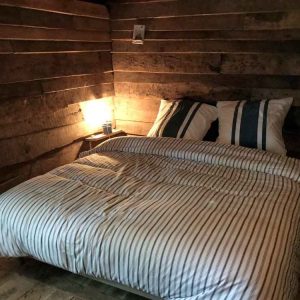 Chalet en bois au Limousin, lit douillet avec draps rayés et ambiance chaleureuse.