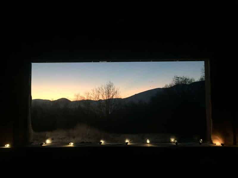 Vue depuis un chalet avec des lumières, offrant un panorama sur les montagnes au coucher du soleil.