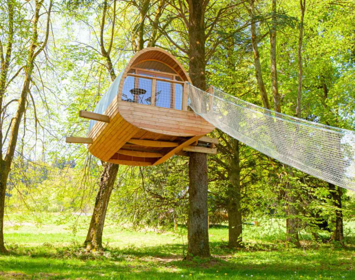 Cabane perchée dans les arbres, entourée de verdure et dun hamac suspendu.