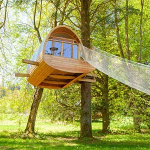 Cabane perchée dans les arbres, entourée de verdure et dun hamac suspendu.