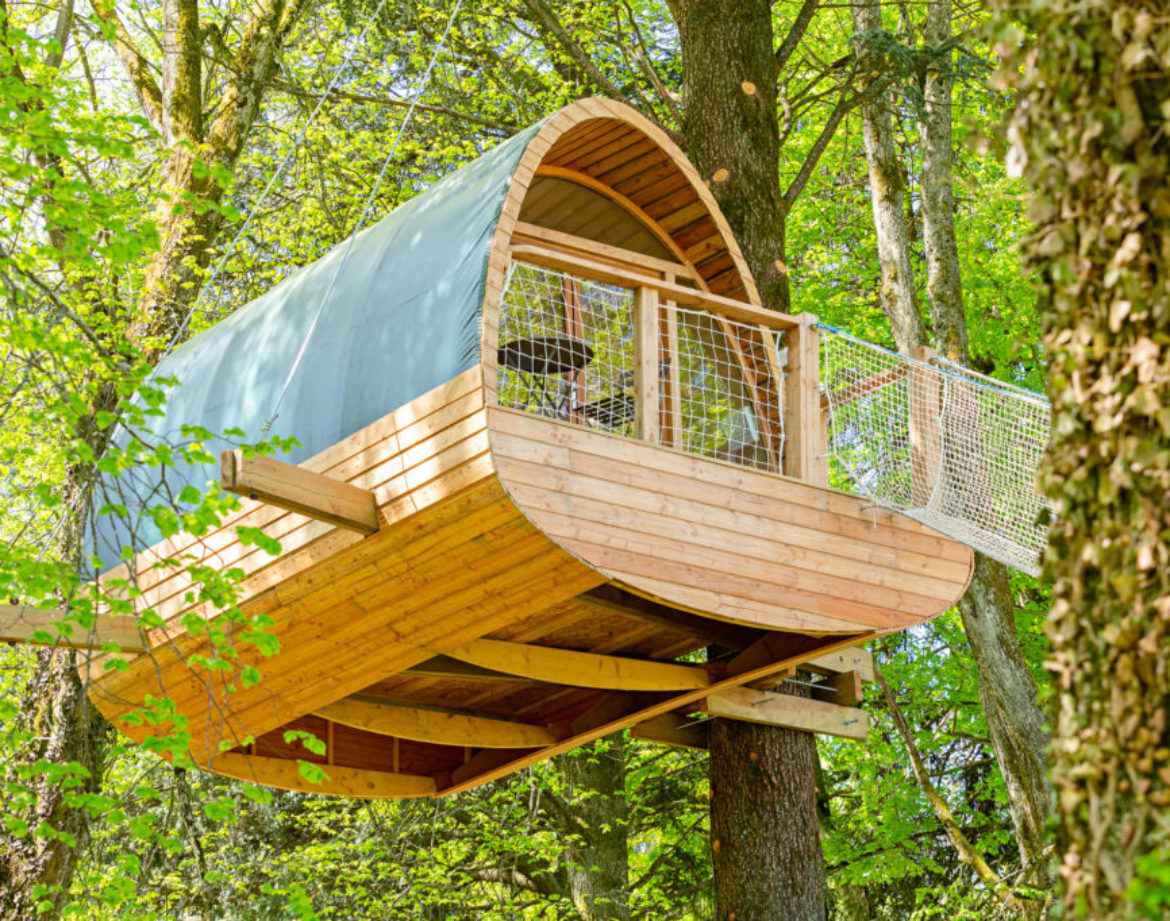 Cabane perchée en bois dans les arbres, entourée de verdure luxuriante.