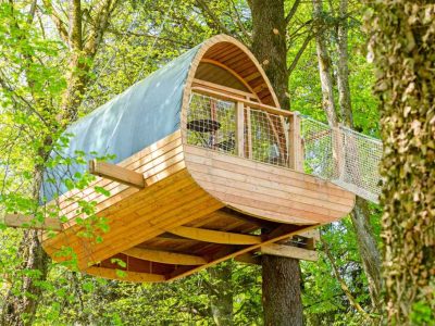 Cabane perchée en bois dans les arbres, entourée de verdure luxuriante.