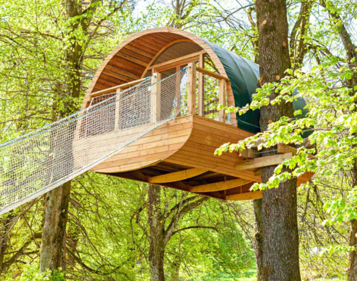 Cabane perchée en bois dans les arbres, entourée de verdure luxuriante.