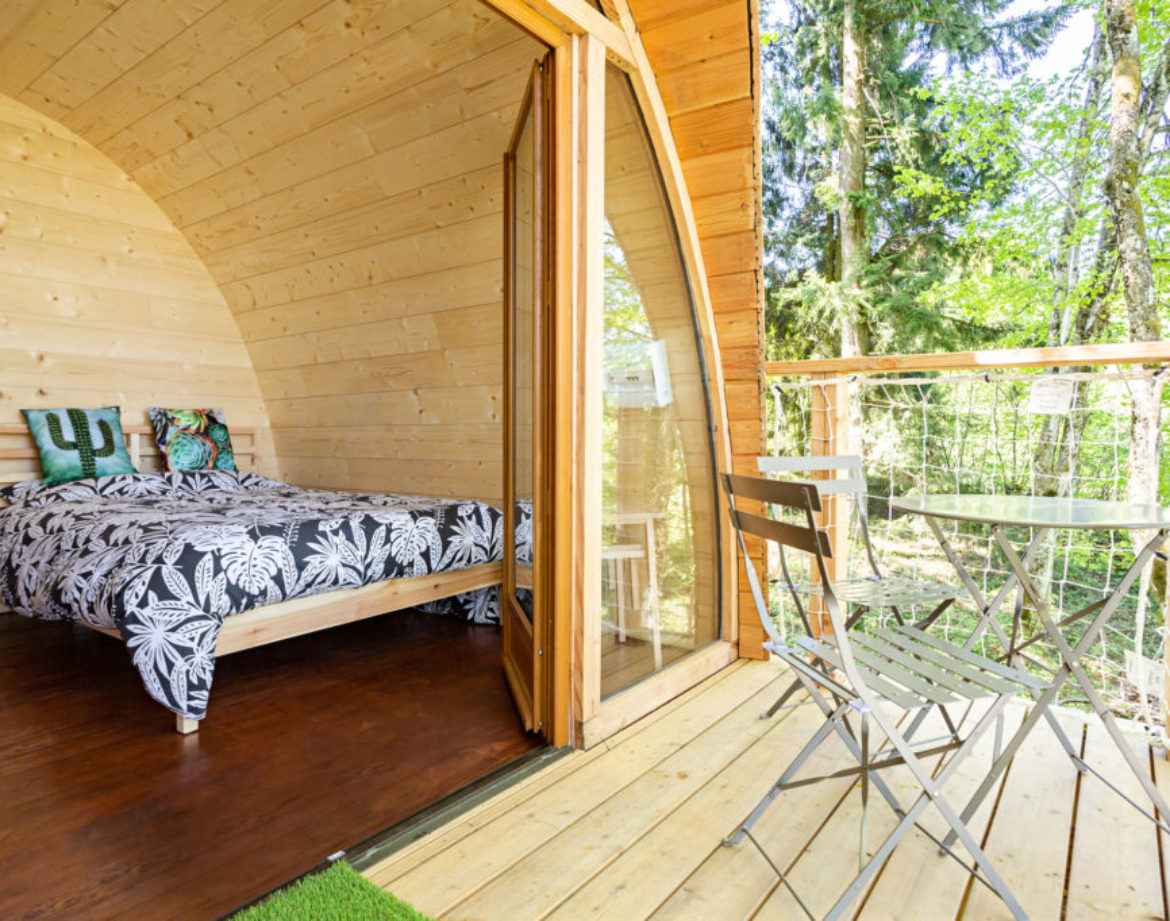 Cabane en bois avec lit douillet et terrasse en bois, entourée de verdure.