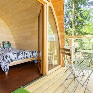 Cabane en bois avec lit douillet et terrasse en bois, entourée de verdure.