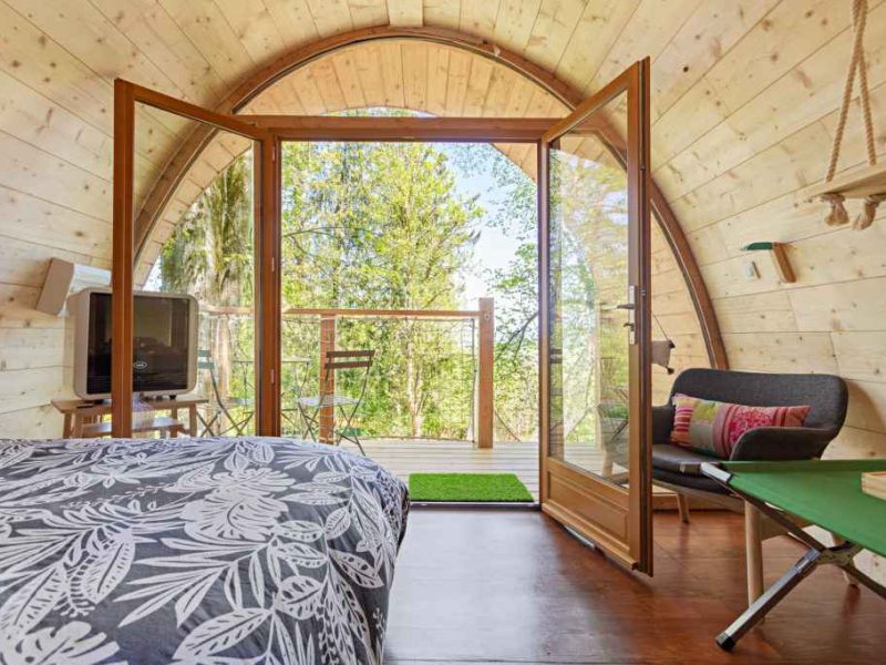 Chalet en bois avec grandes baies vitrées et vue sur la nature verdoyante.
