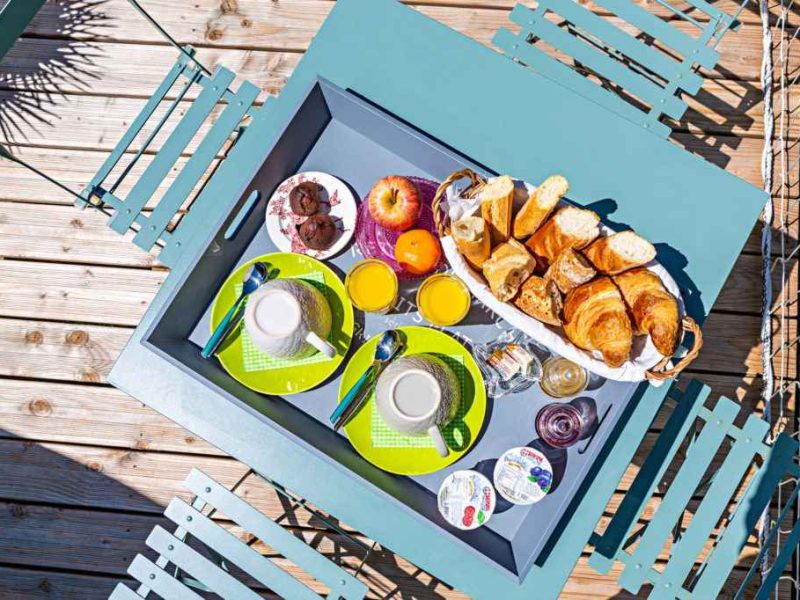 Petit-déjeuner copieux sur une terrasse en bois, avec croissants et jus dorange.