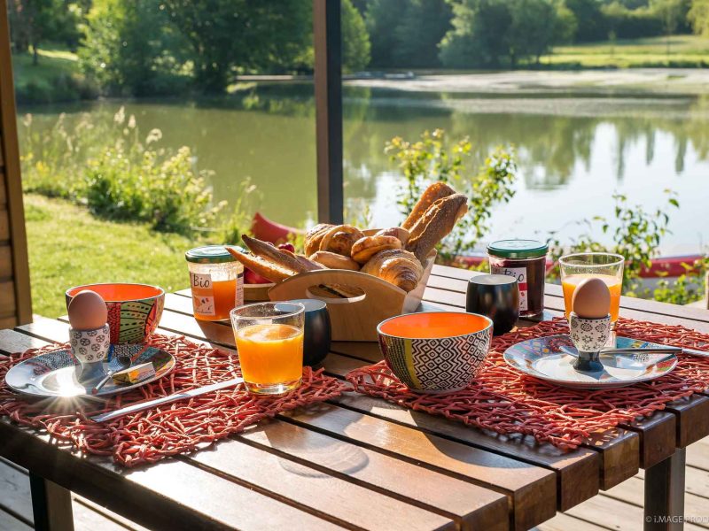 Chalet au bord de leau avec un petit-déjeuner coloré sur la terrasse ensoleillée.