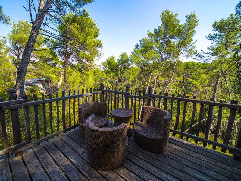 Terrasse en bois avec fauteuils en rotin, vue sur la forêt environnante.