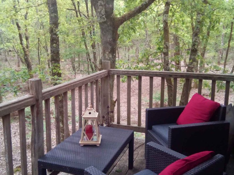 Terrasse dun chalet en bois, avec fauteuils confortables et lanternes, entourée de verdure.