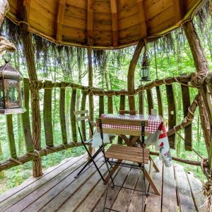 Cabane perchée en bois avec une table à manger et des lanternes dans les arbres.