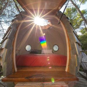 Hébergement insolite en forme de cabane avec lumière du soleil et lit douillet.