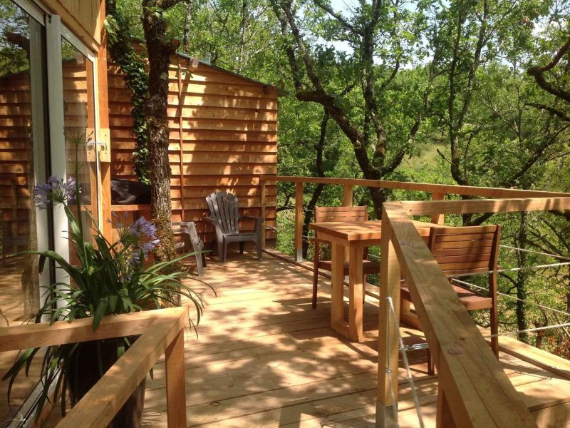 Cabane dans les arbres avec terrasse en bois entourée de verdure.