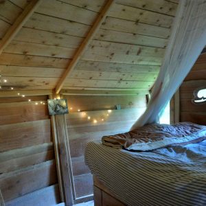 Cabane en bois cosy à Champagne-Ardenne, avec lit confortable et guirlande lumineuse.