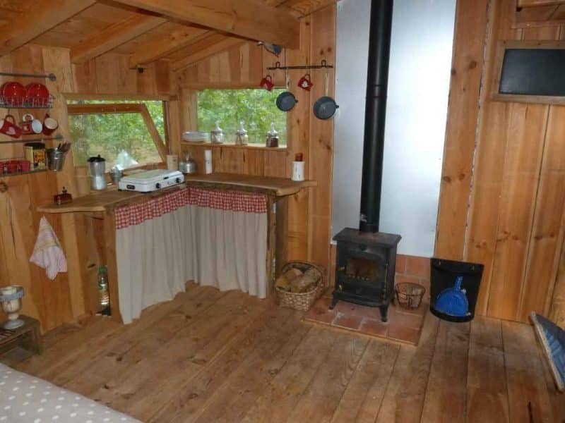 Cabane en bois chaleureuse avec coin cuisine et poêle à bois. Ambiance cosy et naturelle.