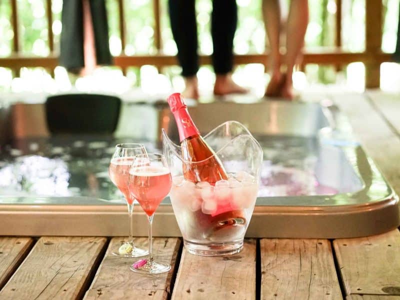 Hébergement en chalet avec jacuzzi, champagne et verres sur une terrasse en bois.