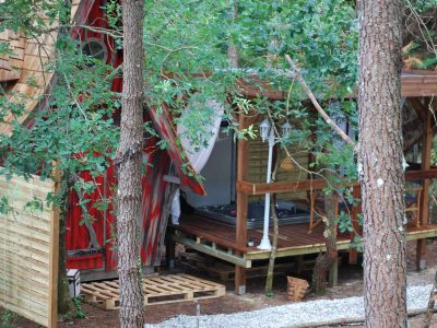 Cabane perchée en Aquitaine, entourée darbres, avec terrasse et jacuzzi.