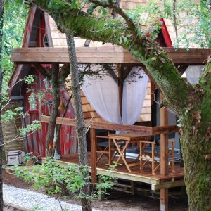 Cabane perchée en Aquitaine, entourée darbres, avec terrasse en bois accueillante.