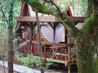 Cabane perchée en Aquitaine, entourée darbres, avec terrasse en bois accueillante.